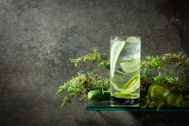 Gin and Tonic with ice, lime, cucumber, and juniper. Iced drink in a misted glass on an old stone background. Copy space.  - Fotografie, Obrázek