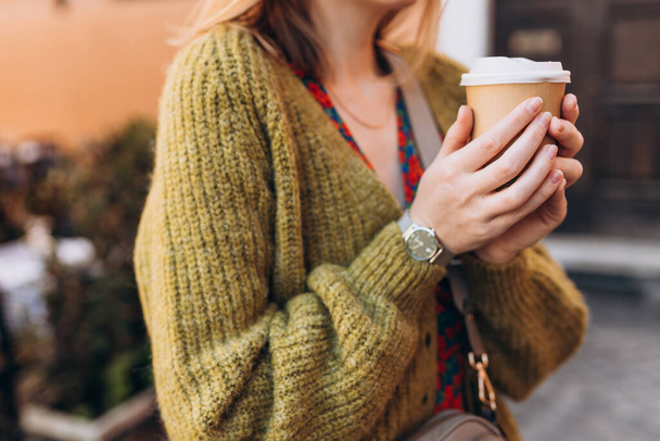 Female hands holding disposable coffee cup on urban background, close up, copy space. Drinking take away coffee. - 写真・画像