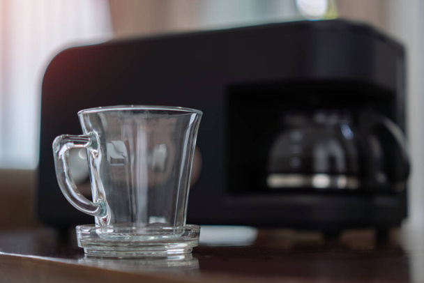 グラスティーポット付きのブラックドリップ電気コーヒーマシンの前に透明なコーヒーマグカップの選択的な焦点は、朝の飲み物を醸造します. - 写真・画像