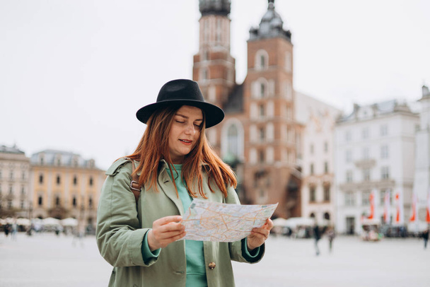Atrakcyjna młoda turystka poznaje nowe miasto. Rudowłosa dziewczyna chodząca i trzymająca papierową mapę w Krakowie. Wiosną podróżuje po Europie. Koncepcja miejskiego stylu życia - Zdjęcie, obraz