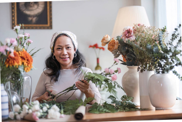 Feliz e atraente mulher asiática madura desfrutando com sua oficina de arranjo de flores on-line em casa... - Foto, Imagem