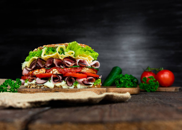 Sandwich with ham, salad, cheese and tomatoes on wooden rustick surface. Copy space, add text - Photo, Image