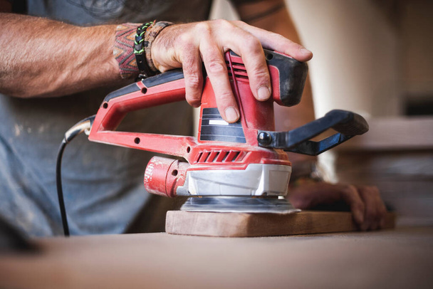 Experience the craftsmanship unfold as a skilled craftsman employs a random orbital sander to meticulously polish and enhance the wood's natural beauty, revealing its true allure. - Photo, Image