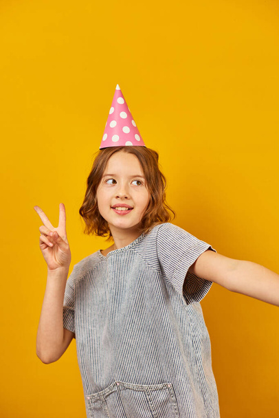 Joyeux, positif dix ans anniversaire fille en chapeau de fête, heureux, sur fond de studio jaune. - Photo, image