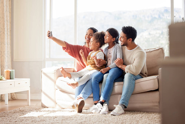 Родители, дети и диван селфи с улыбкой, счастье и связь в гостиной для приложения социальных медиа. Отец, мать и дочери с заботой, любовью и вместе для профиля фото, блог и счастливый на диване. - Фото, изображение