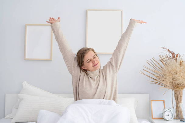 белая женщина просыпается в своей постели по утрам. Молодая женщина тысячелетия делает свою утреннюю рутину в спальне - Фото, изображение