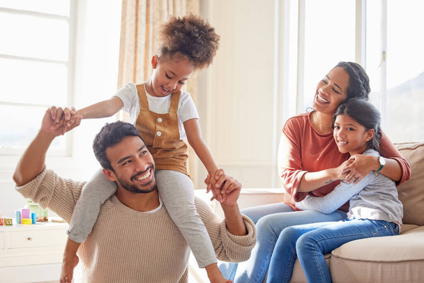 Dad, mom and children in home, shoulders and happiness with playing games, hug or bonding in lounge. Father, mother and daughter with care, love and together with embrace, quality time or living room. - 写真・画像