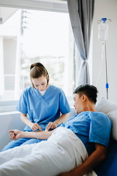  Friendly Female  Nurse Making  Checkup on Patient  in Bed. She Checks tablet while Man Fully Recovering after Successful Surgery in a hospital - Photo, image
