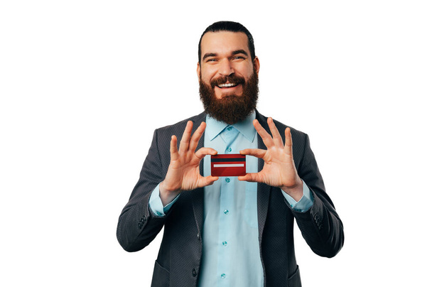 Happy bearded business man wearing jacket is holding the new red credit card he has just got. - Fotoğraf, Görsel