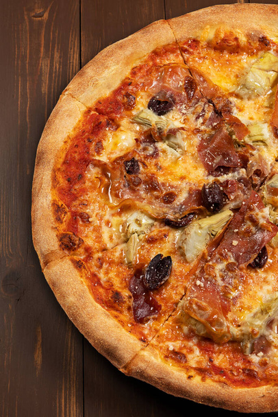 Pizza with tomato sauce, mixed cheese selection, ham, pepperoni, bacon, fresh mushrooms and olives on wooden background. - Фото, зображення