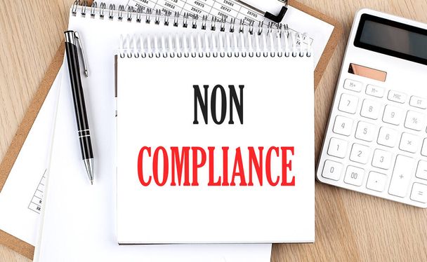 NON COMPLIANCE is written in a white notepad near a calculator, clipboard and pen. Business concept - Photo, Image