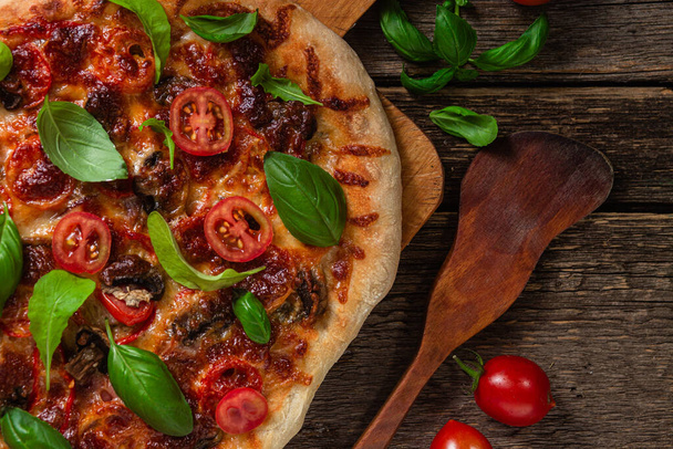 Apetyczna pizza. Pizza z szynką, grzybami i pomidorami na drewnianym tle - Zdjęcie, obraz