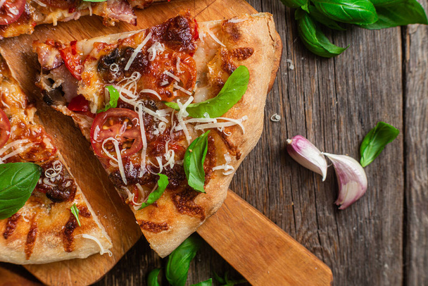 Appetizing pizza. Pizza with ham,mushrooms and tomatoes on a wooden background - Photo, Image