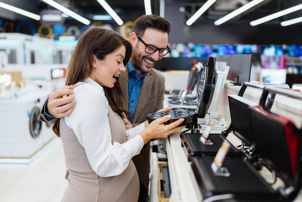 Beautiful and happy middle age couple buying consumer tech products in modern home tech store. They are choosing small kitchen appliances. People and consumerism concept. - Фото, зображення