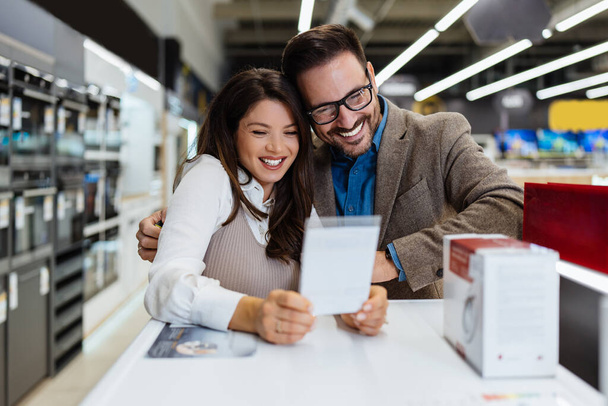 Beautiful and happy middle age couple buying consumer tech products in modern home appliances store. They are choosing washing or cloth dryer machine. People and consumerism concept. - Фото, зображення