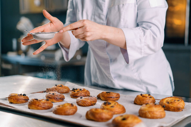 привлекательный пекарь посыпать порошок сахара готов свежеиспеченные горячие ароматные булочки выпечки производства хлебобулочной - Фото, изображение