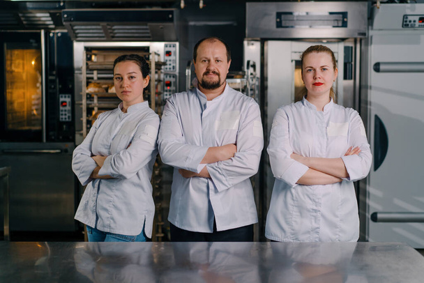 μια ομάδα από χαμογελαστούς επαγγελματίες αρτοποιούς σε μια επαγγελματική κουζίνα σε ένα φούρνο πριν από την έναρξη της παραγωγής ψησίματος - Φωτογραφία, εικόνα