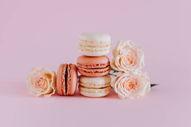 Tasty french macarons with tender rose flowers on a pink pastel background. Place for text. - 写真・画像