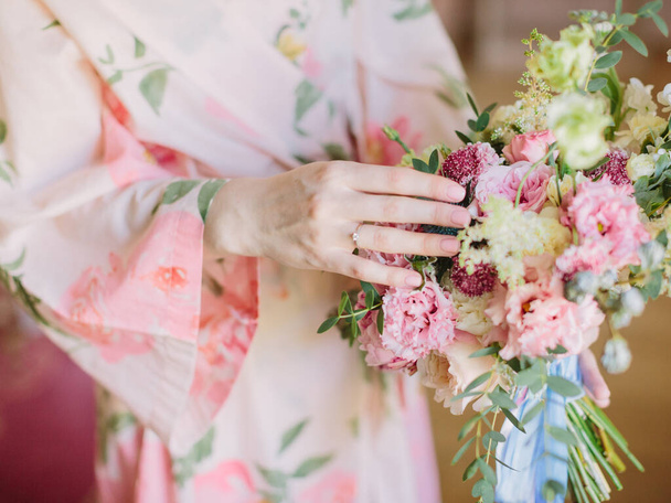 Çiçekli pembe bornozlu bir gelin elinde pembe bir düğün buketi tutuyor. Düğün yüzüğü gelinin parmağında.. - Fotoğraf, Görsel