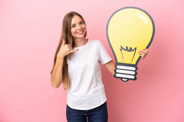 Young Lithuanian woman isolated on pink background holding a bulb icon and doing phone gesture - Foto, Bild