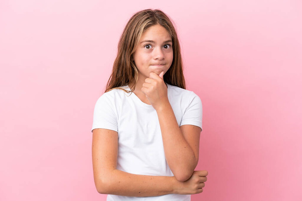 Little caucasian girl isolated on pink background having doubts and thinking - 写真・画像