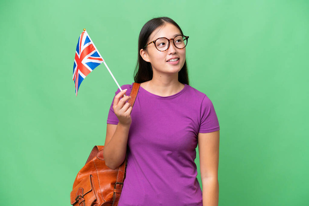 Junge Asiatin mit britischer Flagge vor isoliertem Hintergrund, die eine Idee denkt, während sie nach oben blickt - Foto, Bild