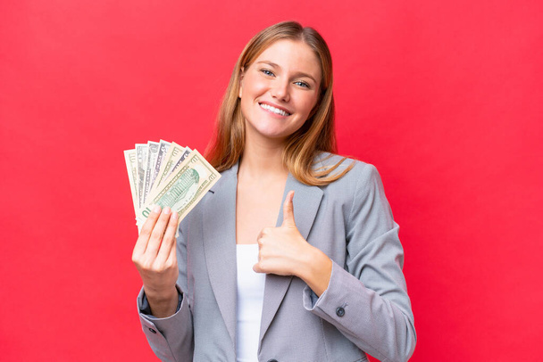 Nuoret liike valkoihoinen nainen tilalla rahaa eristetty punaisella taustalla antaa peukalot ylös ele - Valokuva, kuva