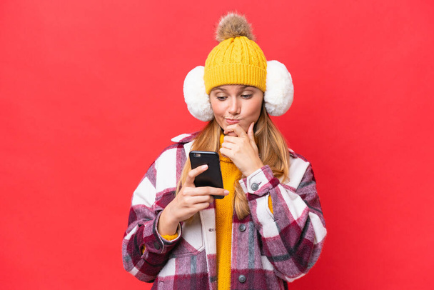 Jovem mulher bonita vestindo regalos de inverno isolado no fundo vermelho pensando e enviando uma mensagem - Foto, Imagem