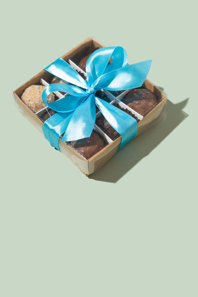 Gift box with ribbon bow with chocolate craft candies inside on green background. - Φωτογραφία, εικόνα