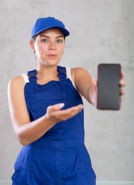 Cheerful female worker in overalls showing screen of her phone - Foto, Imagen