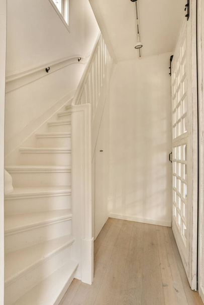 интерьер дома с деревянным полом и белыми окрашенными стенами, лестницей, ведущей на второй этаж - Фото, изображение