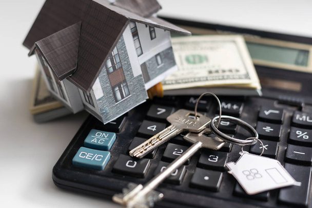 Una casa modelo sentada con una calculadora y billetes de veinte dólares sobre un fondo blanco con ruta de recorte, calculadora de hipotecas - Foto, Imagen