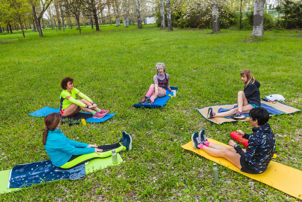 Group of mature ladies exercising outdoors on the grass of a meadow with towels and mats. Hydration concept with metal eco water bottles - Foto, Imagem