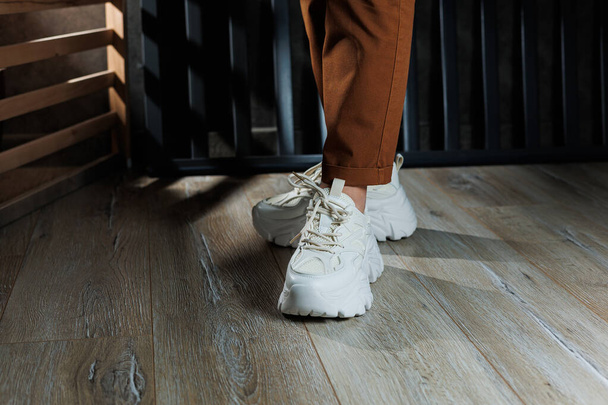 Detailní záběr ženských nohou v bílých kožených teniskách s vysokými podrážkami. Kolekce letních dámských bot. Bílé dámské tenisky s tkaničkou - Fotografie, Obrázek