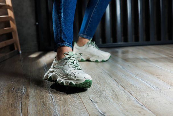 Sports shoes for women. Slender female legs in jeans and white stylish casual sneakers. Comfortable women's summer shoes. Casual women's fashion. - Fotografie, Obrázek