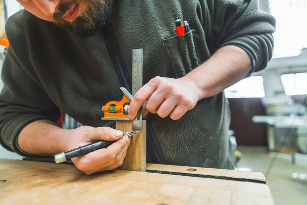Χέρια του αρσενικού ξυλουργού γραμμή σχεδίασης χρησιμοποιώντας δείκτη και χάρακα πριν από την κοπή ξύλου. Υψηλής ποιότητας φωτογραφία - Φωτογραφία, εικόνα