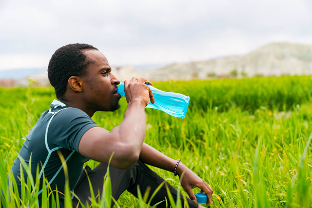 Tiro de un joven deportivo bebiendo agua mientras corre por la naturaleza - Foto, imagen