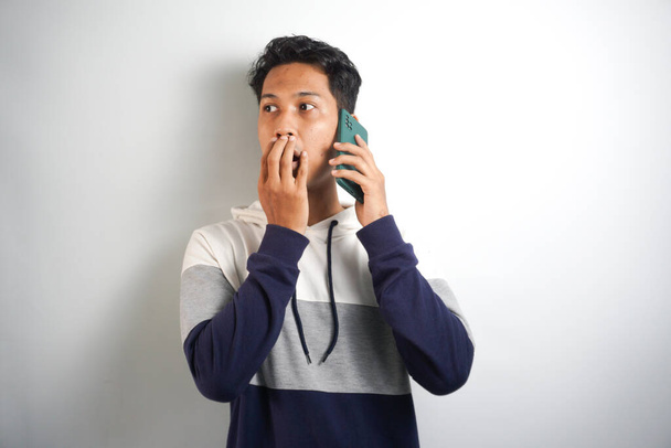Young handsome man speaking on the phone over isolated background cover mouth with hand shocked - 写真・画像
