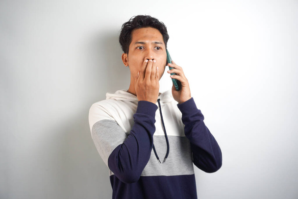 Young handsome man speaking on the phone over isolated background cover mouth with hand shocked - Foto, Imagem