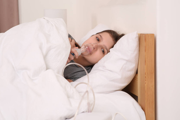 Cute girl using nebulizer for inhalation on bed at home - Foto, afbeelding