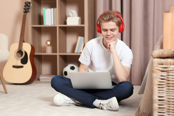 Online learning. Smiling teenage boy in headphones with laptop at home - Fotó, kép