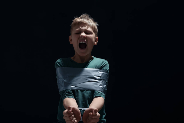 Scarred little boy tied up and taken hostage on dark background - Photo, Image