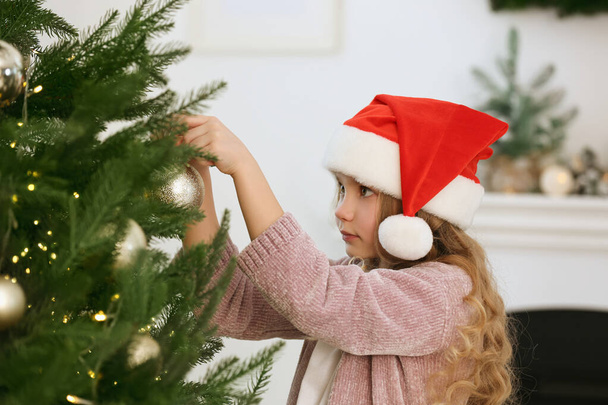 Cute little girl decorating Christmas tree at home - Fotó, kép