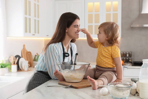 Mother and her little daughter cooking dough together in kitchen - Photo, Image