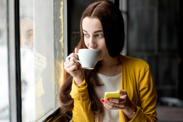 Mulher com telefone e uma xícara de café
 - Foto, Imagem