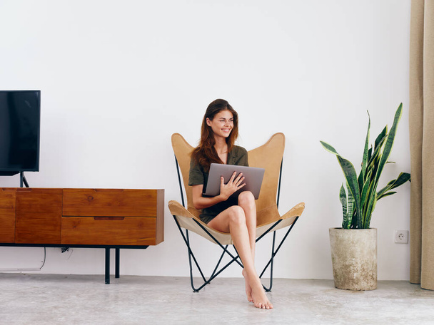 Γυναικεία σπουδαστική μελέτη κάθεται σε μια καρέκλα με ένα φορητό υπολογιστή εργασίας στο σπίτι χαμόγελο, μοντέρνο κομψό εσωτερικό σκανδιναβικό τρόπο ζωής, αντίγραφο χώρου. Υψηλής ποιότητας φωτογραφία - Φωτογραφία, εικόνα