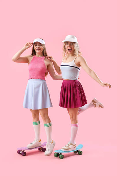 Hermanas jóvenes con monopatines sobre fondo rosa - Foto, Imagen