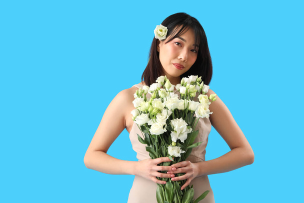 Bella donna asiatica che tiene bouquet di fiori di eustoma su sfondo blu - Foto, immagini