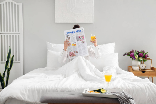 Mañana de mujer joven con vaso de jugo leyendo el periódico en el dormitorio - Foto, Imagen