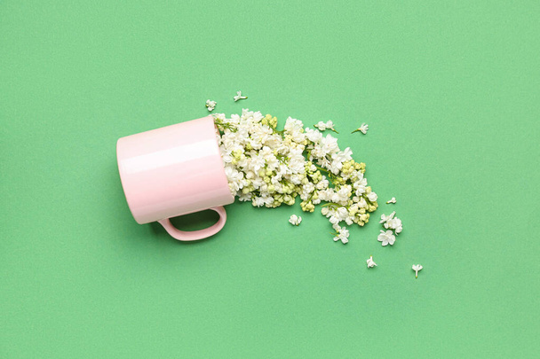 опрокинутая чашка с белыми сиреневыми цветами на зеленом фоне - Фото, изображение